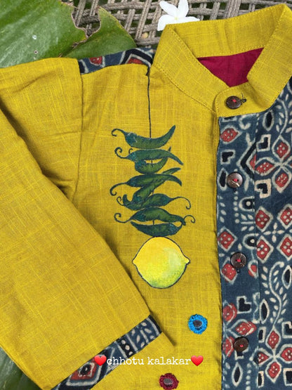 Kids traditional outfit showing a mustard yellow and indigo blue Ajrakh print kurta with handpainted mirror work, nimbu-mirchi illustration, 100% DeSi text, and white pyjamas.