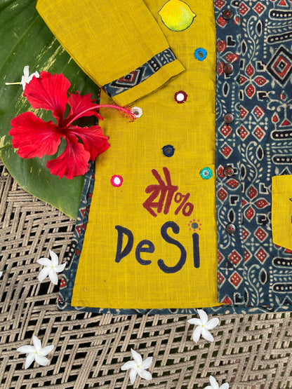 Kids traditional outfit showing a mustard yellow and indigo blue Ajrakh print kurta with handpainted mirror work, nimbu-mirchi illustration, 100% DeSi text, and white pyjamas.