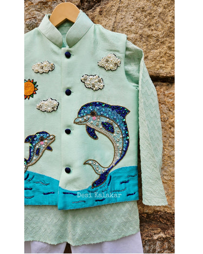 "Three-piece boys' festive outfit featuring a sea green hand-embroidered dolphin jacket layered over a matching textured zig-zag kurta and classic white pants."