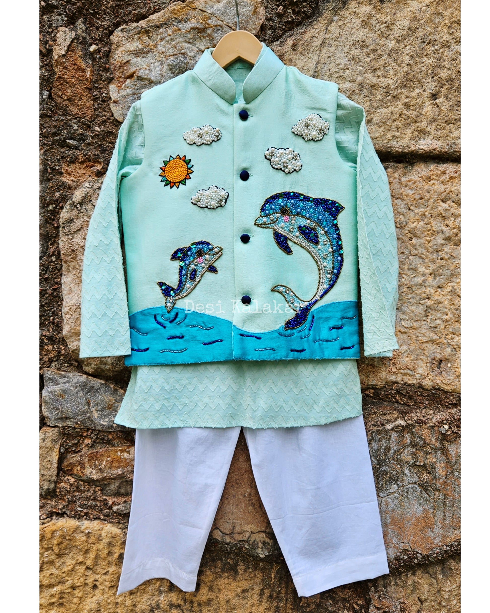 "Three-piece boys' festive outfit featuring a sea green hand-embroidered dolphin jacket layered over a matching textured zig-zag kurta and classic white pants."