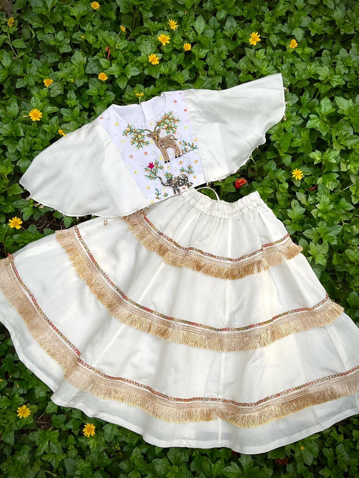 Little girl wearing a handcrafted ivory zardozi embroidered top and tiered fringe lehenga set by Desi Kalakar.