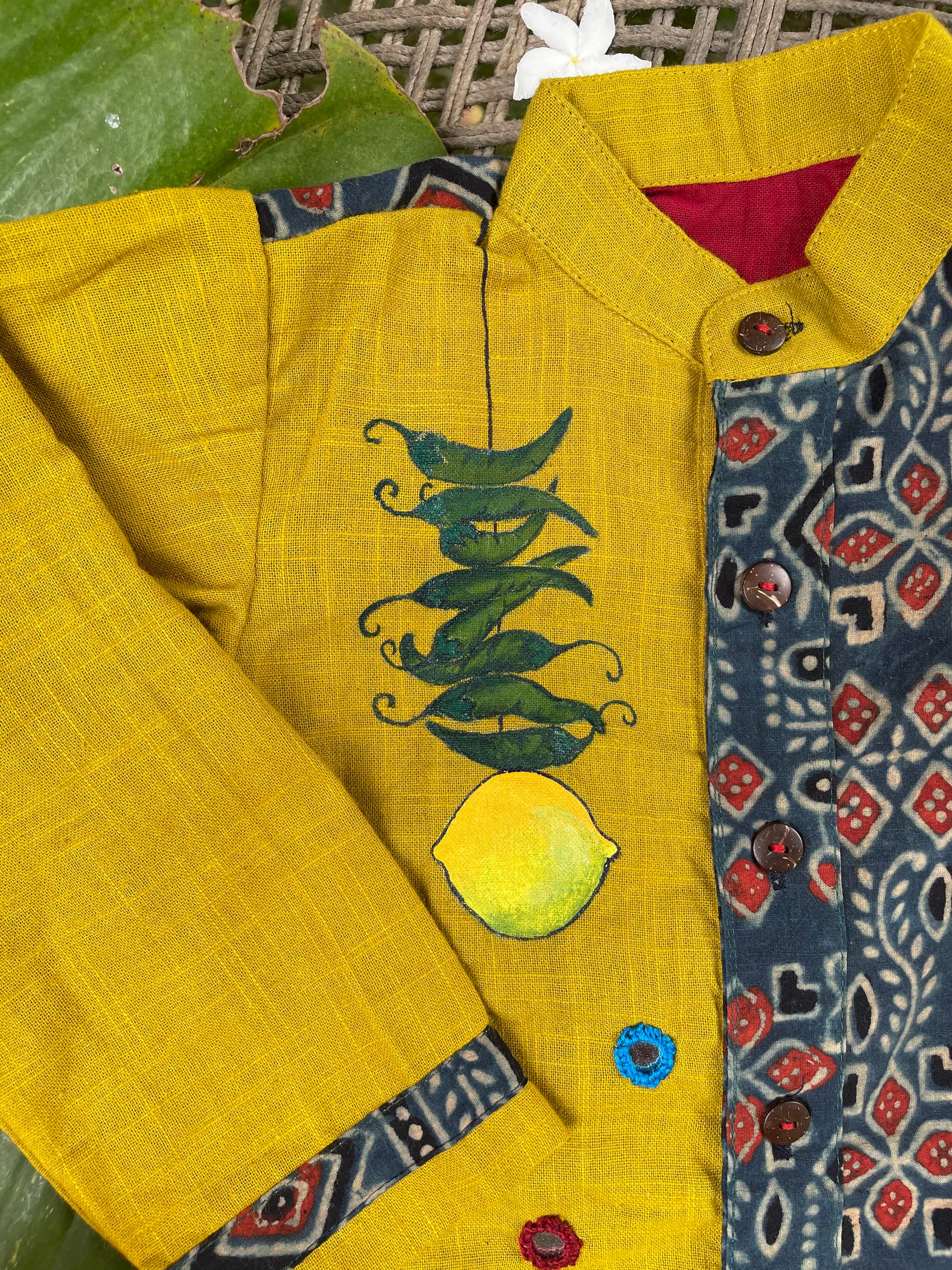Kids traditional outfit showing a mustard yellow and indigo blue Ajrakh print kurta with handpainted mirror work, nimbu-mirchi illustration, 100% DeSi text, and white pyjamas.