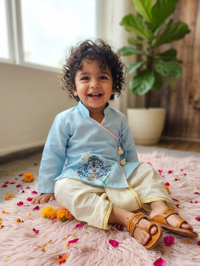 Little boy wearing a sky blue hand-embroidered Shiva Angrakha kurta with cream-colored dhoti pants."