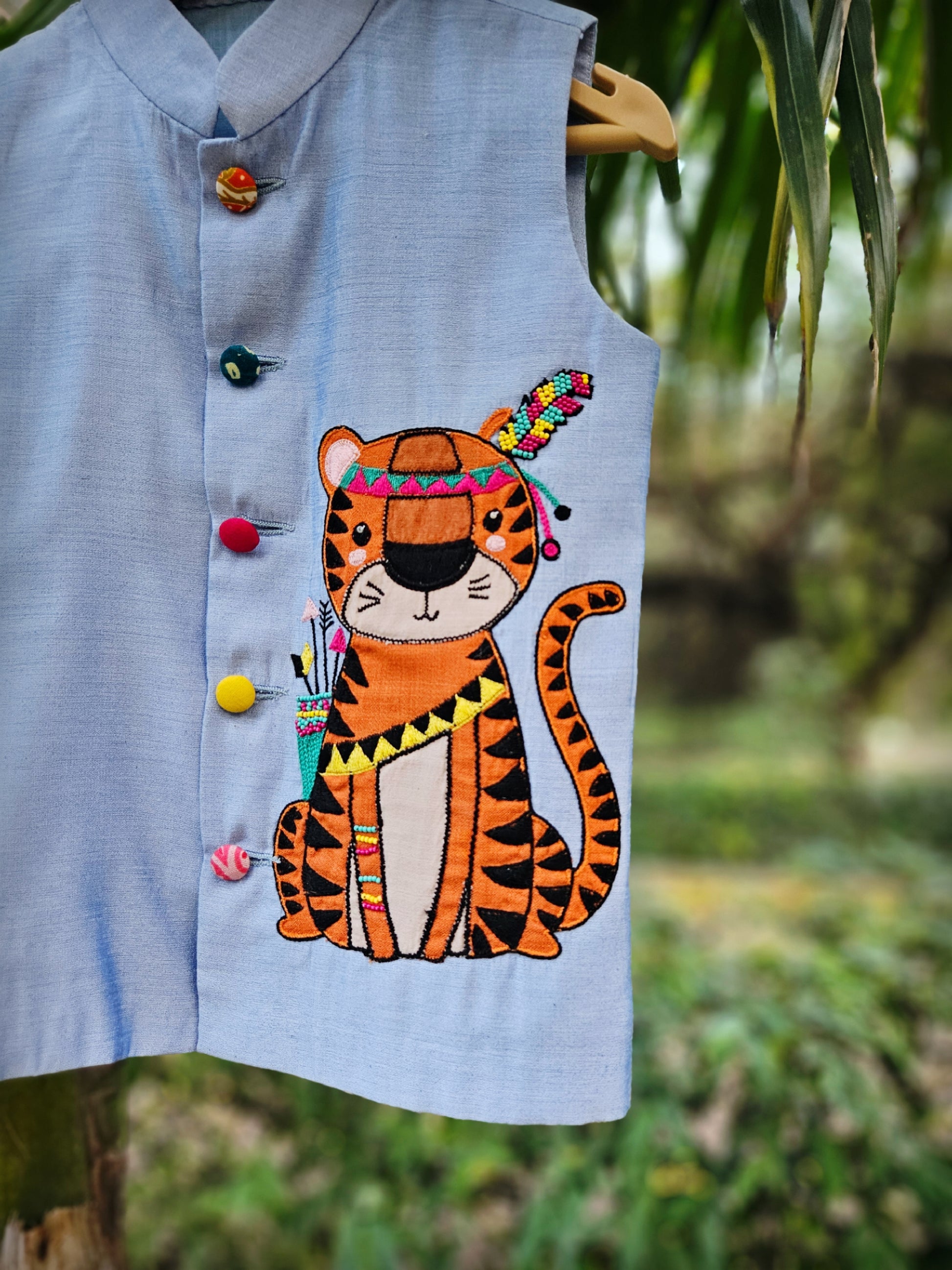 "Premium powder blue handcrafted Bundi Nehru jacket for boys featuring a large hand-embroidered tribal tiger motif with a colorful feather headpiece."