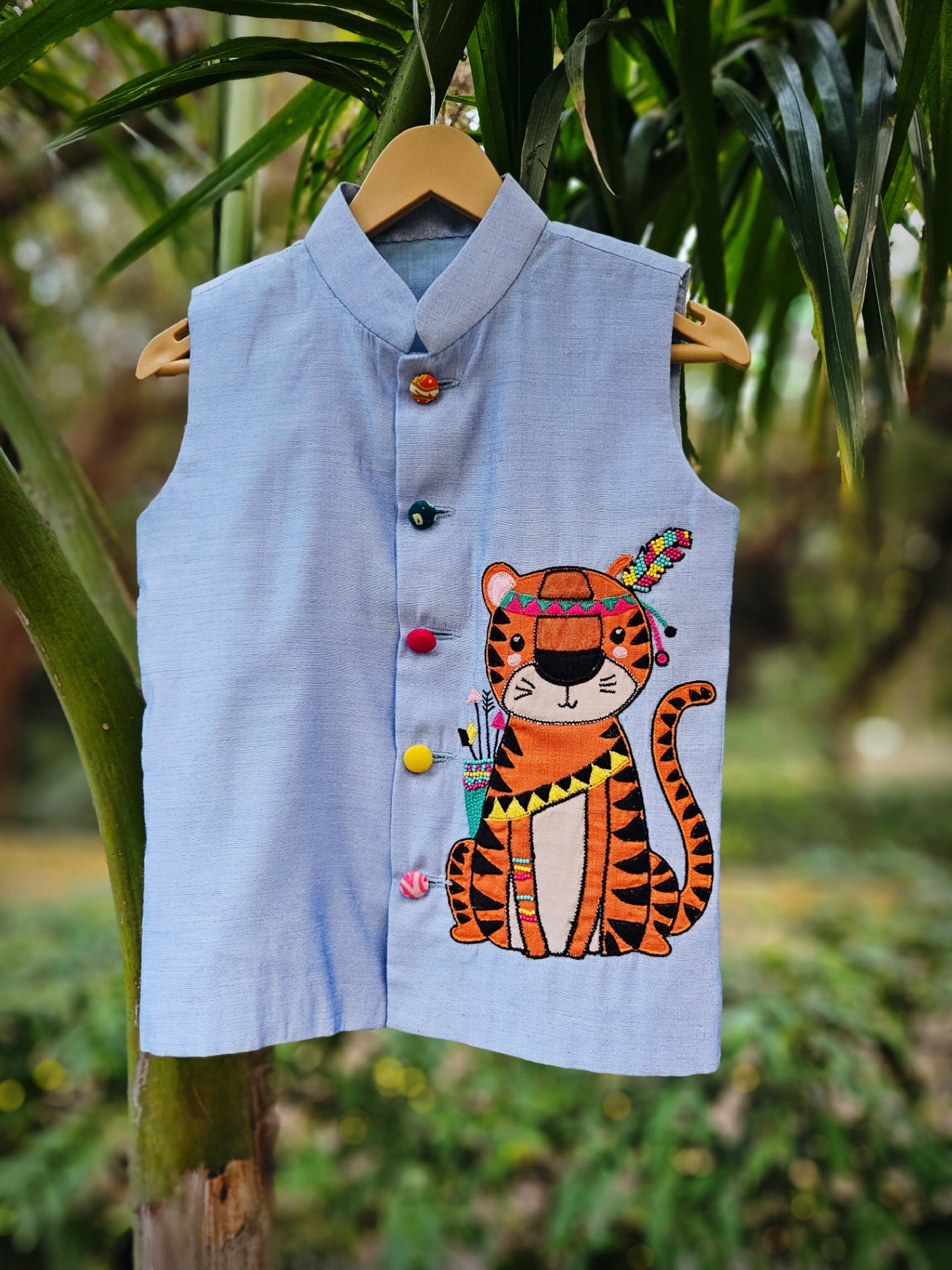 "Premium powder blue handcrafted Bundi Nehru jacket for boys featuring a large hand-embroidered tribal tiger motif with a colorful feather headpiece."