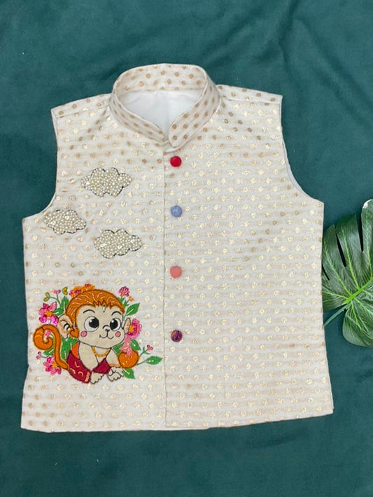 An off-white boys' ethnic Bundi jacket with woven gold zari dots, featuring a hand-embroidered cute baby Hanuman monkey character with pink flowers and three 3D pearl-beaded clouds.