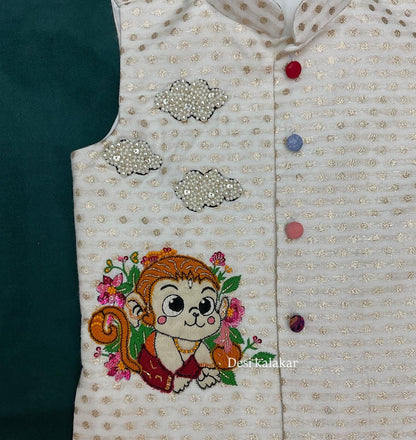 An off-white boys' ethnic Bundi jacket with woven gold zari dots, featuring a hand-embroidered cute baby Hanuman monkey character with pink flowers and three 3D pearl-beaded clouds.