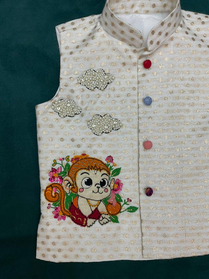 An off-white boys' ethnic Bundi jacket with woven gold zari dots, featuring a hand-embroidered cute baby Hanuman monkey character with pink flowers and three 3D pearl-beaded clouds.