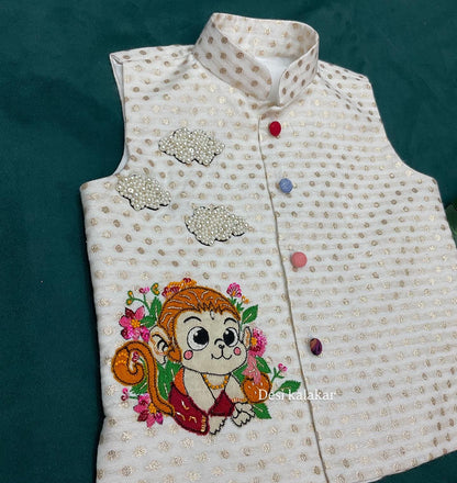 An off-white boys' ethnic Bundi jacket with woven gold zari dots, featuring a hand-embroidered cute baby Hanuman monkey character with pink flowers and three 3D pearl-beaded clouds.