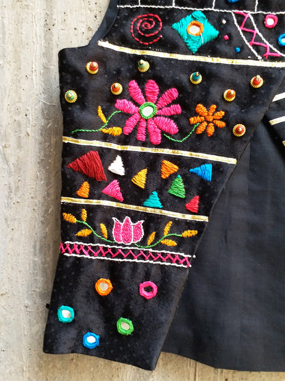 Kids traditional festive wear showing a premium black sleeveless asymmetric Bundi jacket for boys featuring multi-color Kutchi mirror work, floral embroidery, and horizontal gold stripes.